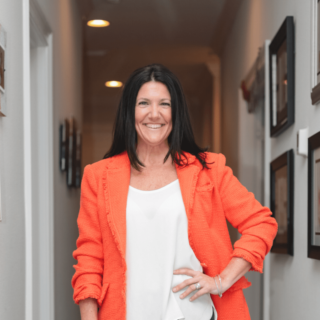 A woman in an orange jacket standing next to a wall.